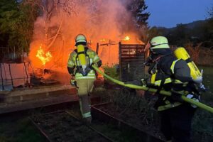 Feuerwehr löscht Brand einer Gartenhütte, Rauchsäule zeigt Einsatzkräften den Weg.