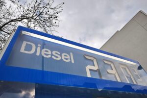Grafik eines Sparmaßnahmen-Symbols vor dem Hintergrund einer Tankstelle und Preisschildern.