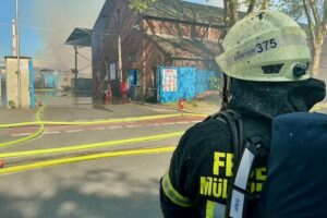 Großbrand mit Rauchsäule, Feuerwehr im Einsatz, brennende Altpapierballen, Rettungsmaßnahmen für Verletzte.