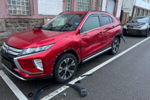 Ein roter Mitsubishi Eclipse mit Schäden, Parkplatzsituation, Polizeiaufruf zur Zeugenmeldung.