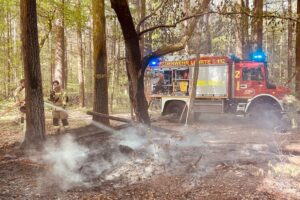 Brennendes Holz-Tipi im Wald, Feuerwehr löscht Glutnester, erhöhte Waldbrandgefahr aufgrund Trockenheit.