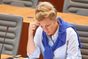 Kulturministerin Ina Brandes steht vor einem Museum, umgeben von historischen Artefakten und Forschern.