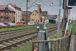LKW-Fahrer beschädigt Schranke am Bahnübergang, verursacht Zugverspätungen, Polizei ermittelt.
