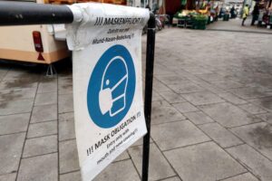 Gesundheitskrise: Menschen mit Long Covid und ME/CFS auf Wochenmarkt, Maskenpflicht symbolisiert Herausforderung.