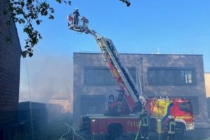 Feuerwehrmänner bekämpfen Brand eines Gewerbebetriebs, Einsatzkräfte und Löschmaßnahmen im Vordergrund.