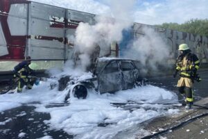 Auto in Flammen auf Autobahn, Feuerwehr im Einsatz, Rauchentwicklung sichtbar, Verkehr behindert.