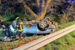 Unfallstelle mit verunfalltem PKW, Feuerwehr im Einsatz, Rettungskräfte behandeln verletzte Personen.