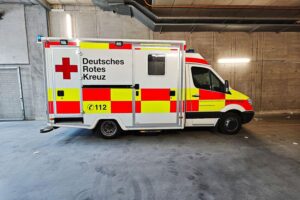 Rettungswagen am Unfallort mit verletzter älterer Frau und zwei Männern, die Hilfe erhalten.