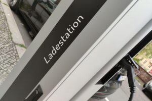 E-Auto Ladestation vor einem Mehrparteienhaus, Symbol für verbesserte Ladeinfrastruktur.