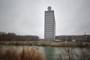 VW-Logo und Fabrikgebäude, symbolisieren Einschnitte und strategische Veränderungen in der Automobilproduktion.