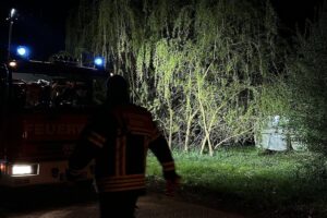 Passant löscht Brand nahe Wohnwagen in Aurich-Wiesens; Feuerwehr kontrolliert mit Wärmebildkamera.