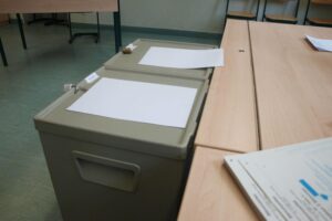 Bild eines Wahllokals mit Wahlurnen und Menschen, die ihre Stimmen abgeben.