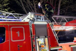 Drehleiter der Feuerwehr vor einem Mehrfamilienhaus, Einsatzkräfte bei Zimmerbrand im dritten Obergeschoss.