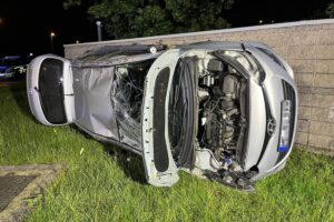 Unfallauto liegt auf der Seite, beschädigte Mauer, Polizeifahrzeuge und Rettungskräfte vor Ort.