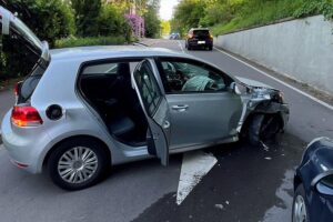 Ein Unfallfahrzeug liegt neben einer Mauer, zwei Personen verletzt, Unfallstelle gesperrt.