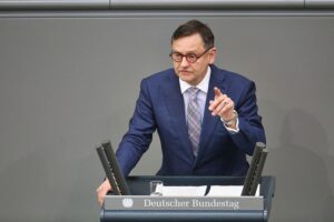 Kay Gottschalk lächelt, umgeben von Wärmepumpe, E-Auto und Solar-Anlage, modern und zukunftsorientiert.