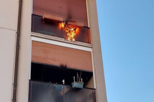 Balkon eines Mehrfamilienhauses mit Feuerwehr im Einsatz bei Brandbekämpfung.