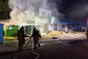 Baucontainerbrand in Remscheid: Feuerwehr bekämpft Flammen, Einsatzkräfte im Einsatz, Garagendach betroffen.