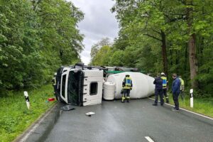 Umgekippter Betonmischer blockiert Landstraße, frischer Beton fließt in den Straßengraben.