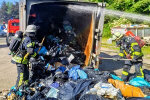 Löscharbeiten an Müllpresse, Feuerwehr im Einsatz, Rauchentwicklung, Klinik in Gefahr, Einsatzkräften vor Ort.