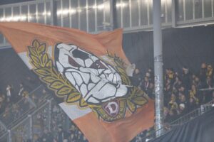 Dynamo-Fans jubeln im Stadion, begleitet von Polizisten, die für Sicherheit sorgen.