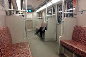 Eine Frau sitzt einsam in der U-Bahn, während dramatische Szenen im Hintergrund geschehen.