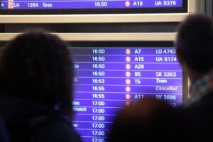 Passagiere schauen besorgt auf Anzeigetafel am Flughafen wegen Flugstreichungen durch Kerosinkrise.