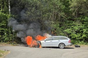 Ein brennendes Auto an der B10 mit Feuerwehr und Polizei im Hintergrund.