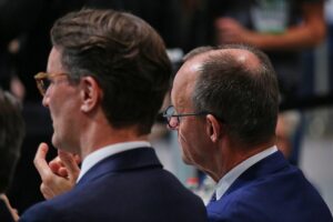 Hendrik Wüst und Friedrich Merz diskutieren zusammen, umgeben von politischen Symbolen und Medien.