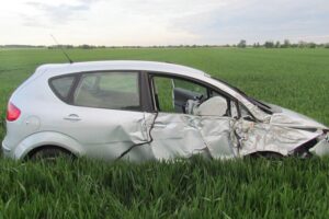 Unfallauto im Feld, Polizei vor Ort, verletzter Fahrer, zerstörtes Fahrzeug, Baumkollision.