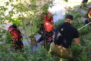 Seniorin im Wasser mit Unterarmstützen, Feuerwehr hilft beim Retten aus gefährlicher Situation.