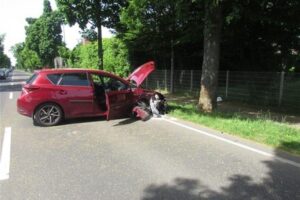 Junge Frau, verletzt nach Unfall mit Baum; schwer beschädigter Toyota, Polizei vor Ort.