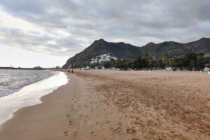 Ein sonniger Strand auf Teneriffa, der entspannte Urlauber trotz globaler Unsicherheiten zeigt.