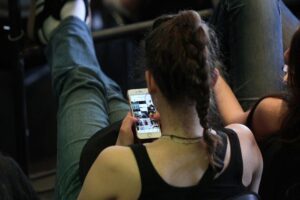 Junge Frau mit Smartphone, nachdenklich, im Kontext von Fake News und Informationsverbreitung.