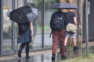 Personen mit Regenschirmen unter wechselhaftem Wetter, Gewitterund Regen in Niedersachsen.