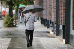 Mann mit Regenschirm unter wechselhaftem Himmel, während Regen und Sonne abwechseln.