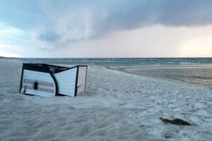 Umgekippter Strandkorb am Strand, symbolisiert unbeständiges Wetter mit Wind und Schauer.