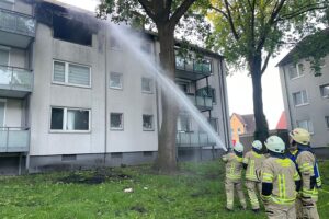 Flammen im Dachbereich eines Wohnhauses, Feuerwehr bei Löscharbeiten sichtbar.