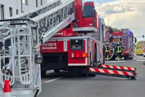 Feuerwehr löscht Zimmerbrand in Mehrparteienhaus; Einsatzkräfte und Rettungsdienst vor Ort.