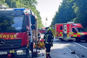 Zwei verunfallte Autos auf Bundesstraße, Rettungsdienste leisten Erste Hilfe am Unfallort.