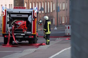 Feuerwehr löscht Brand in Entsorgungsbetrieb, Flammen breiten sich auf Reifenstapel aus.