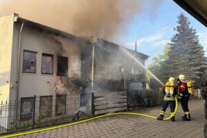 Feuerwehrleute löschen einen großen Brand in einem Industriegebiet, bedrohen angrenzendes Wohngebäude.