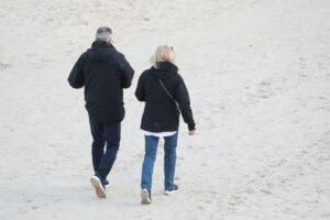 Paar spaziert am Strand, symbolisiert Partnerschaft und soziale Themen in der Gesundheitsversorgung.