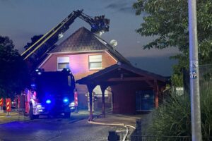 Feuerwehr entfernt Dachpfannen zur Brandbekämpfung in einem Einfamilienhaus nach Dachstuhlbrand.