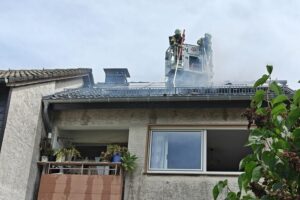 Feuerwehr löscht Brand im Dach eines Wohnhauses, Nachbarn unterstützen evakuierte Bewohner.