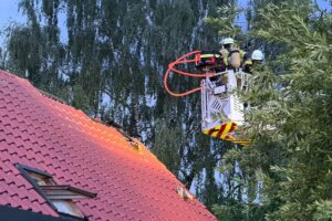 Blitzschlag verursacht Brand im Dach eines Mehrfamilienhauses, Feuerwehr bekämpft offene Flammen.