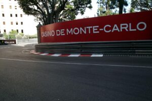 Formel-1-Rennstrecke in Monaco mit jubelndem Publikum und klassischen Autos im Rennbetrieb.