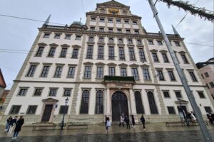 Rathaus Augsburg vor einem Hintergrund von protestierenden Bürgern für bessere Fernverkehrsanbindungen.