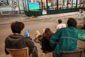 Fußballfans schauen begeistert ein WM-Spiel auf der Straße, Atmosphäre von Lebensfreude und Sportbegeisterung.