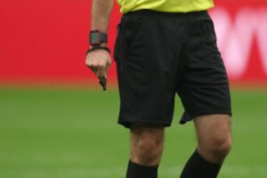 Schiedsrichter zeigt mit Karte auf das Spielfeld während spannendes 2:2-Spiel zwischen Iran und Neuseeland.